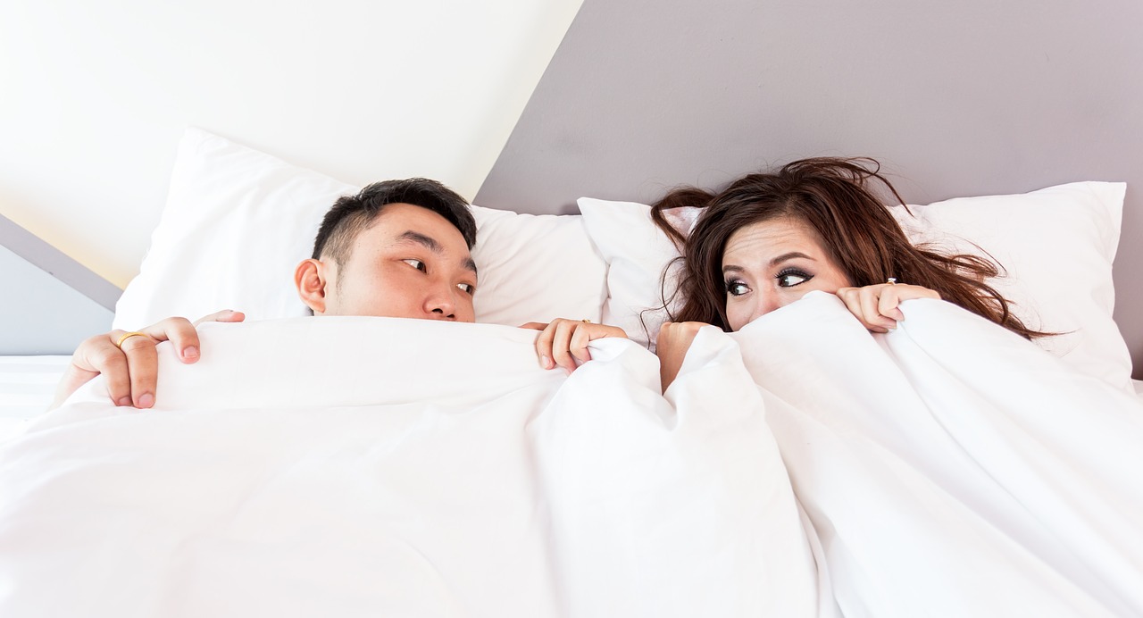 a man and a woman under a white blanket in the bedroom